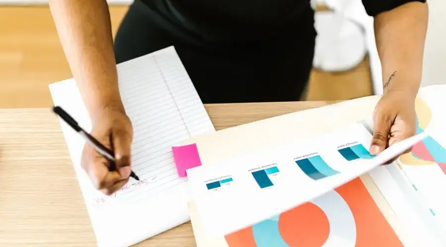 Businesswoman writing notes while analyzing printed graph reports at a desk.