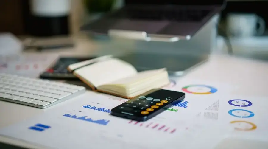 Modern office desk with a laptop, smartphone calculator app, and financial charts.