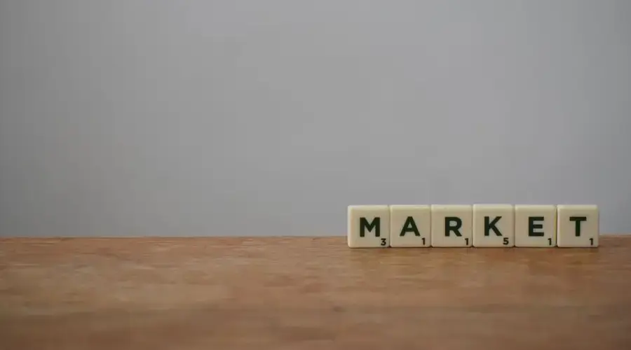 Scrabble tiles spelling 'Market' on a wooden table with a minimalist background.