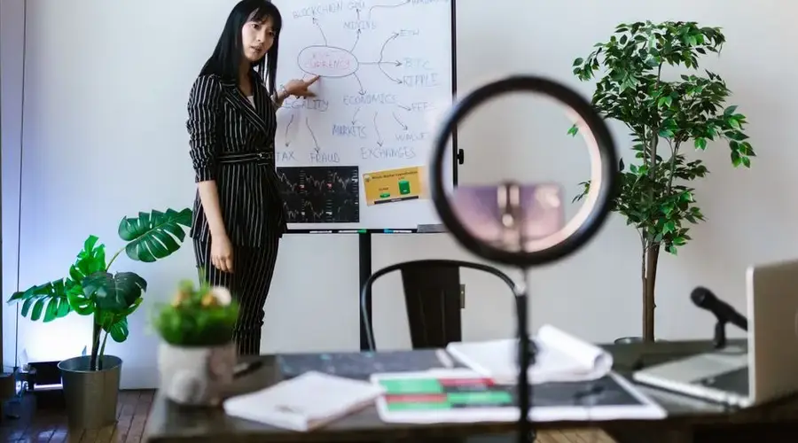 Asian woman presenting cryptocurrency concepts in an office setting with a whiteboard and plants.