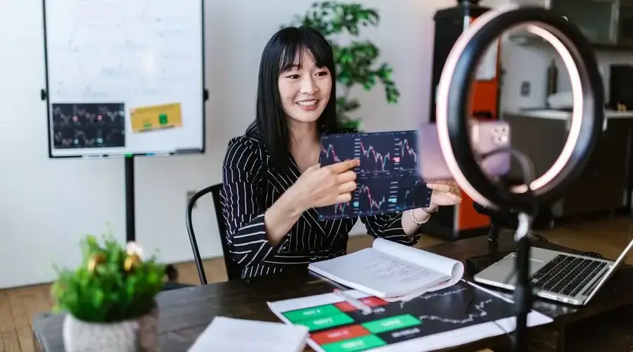 Asian woman discussing cryptocurrency investment during a vlogging session with charts.