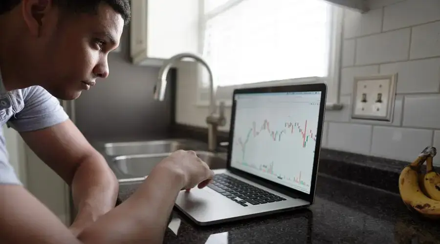 Focused man examining financial graphs on a laptop in a modern kitchen setting.