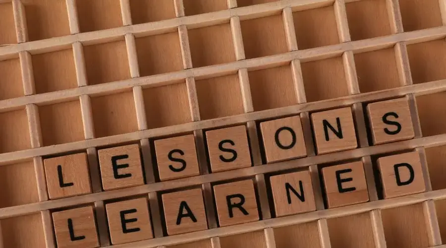 Wooden letter blocks spelling 'lessons learned' on a grid background, symbolizing knowledge and education.
