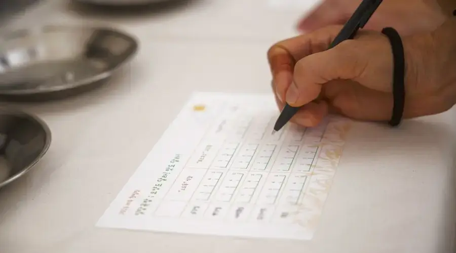 Detailed view of a hand writing on a form with a pen at a table.