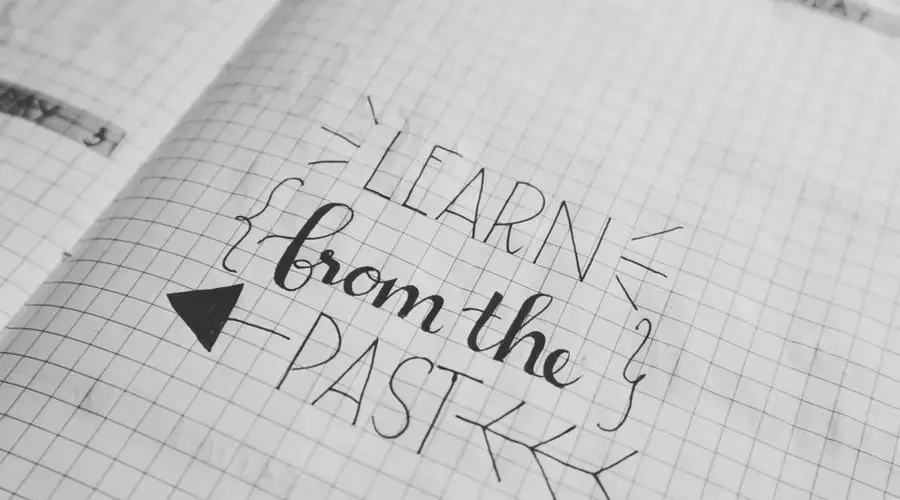 Black and white close-up of a handwritten motivational quote 'Learn from the Past' on graph notebook paper.
