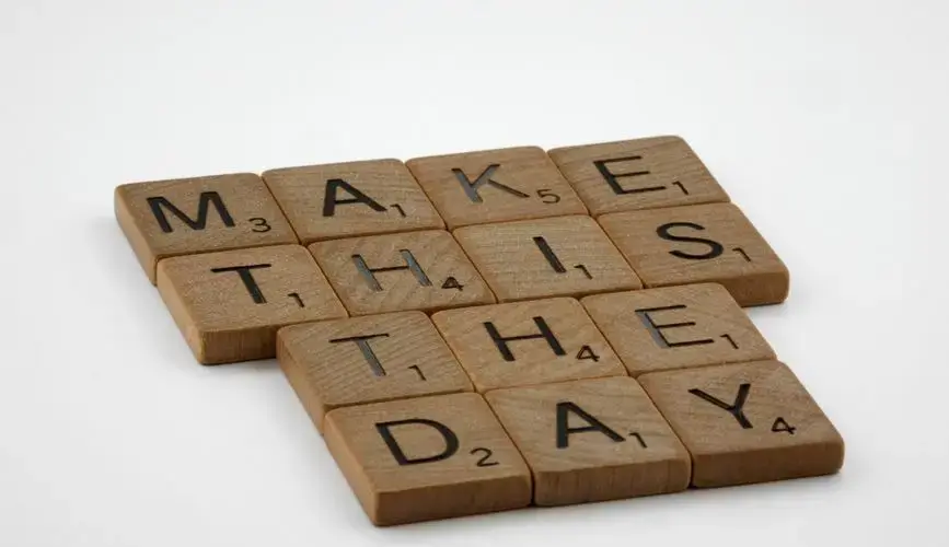 Wooden Scrabble tile pieces arranged to spell 'Make this the day'.
