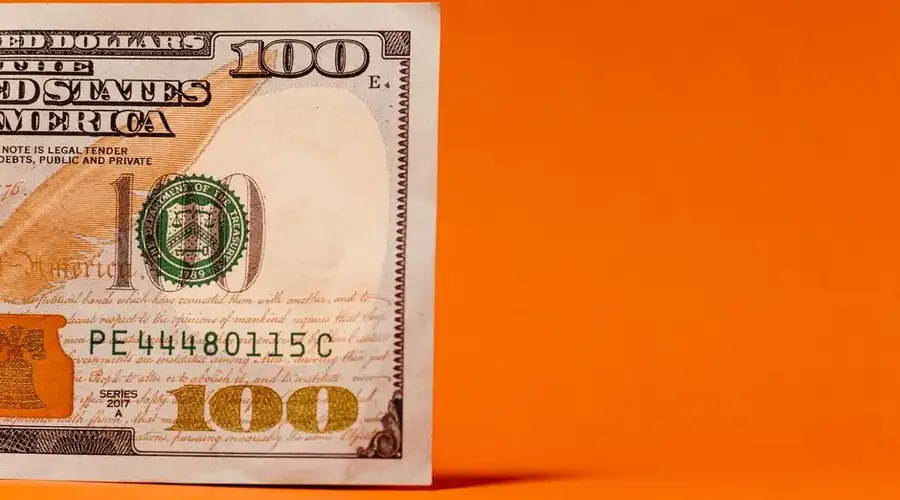 Detailed view of a US 100 dollar bill against a vibrant orange backdrop, highlighting currency concepts.
