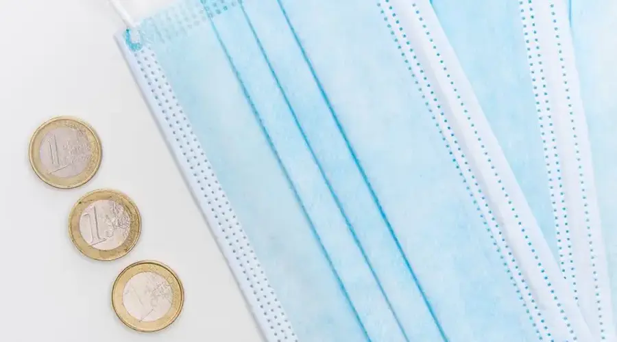 Flatlay of surgical face masks and euro coins, symbolizing pandemic economic challenges.