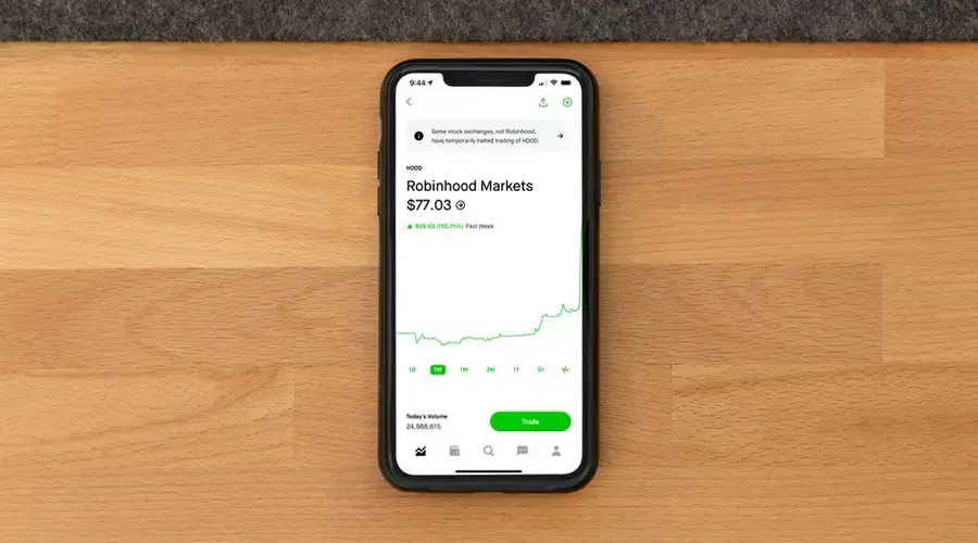 Stock trading app on smartphone displaying Robinhood Markets price on wooden desk.