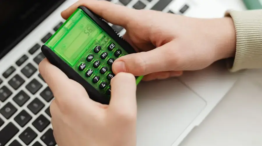 Close-up of hands using a green calculator on a laptop keyboard, indoor setting.