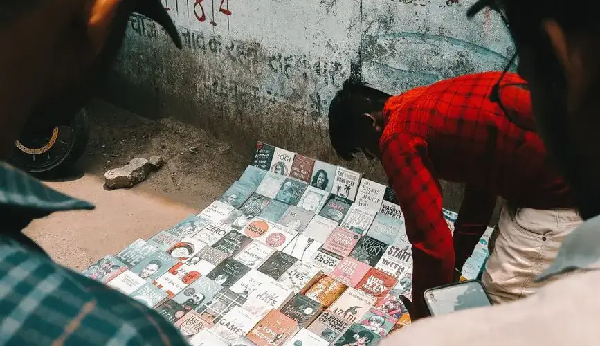 Man selling books on a busy city sidewalk, attracting attention in an urban setting.