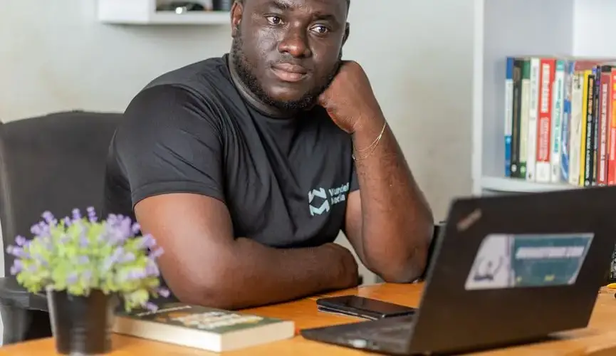 A thoughtful adult man sits at a desk with a laptop, contemplating work.