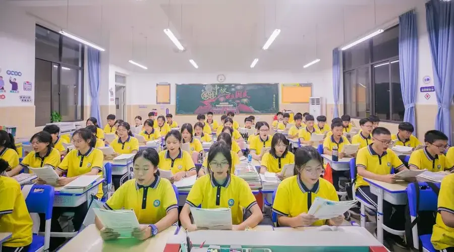 A large group of students in yellow uniforms engaged in classroom activities, reading and learning.