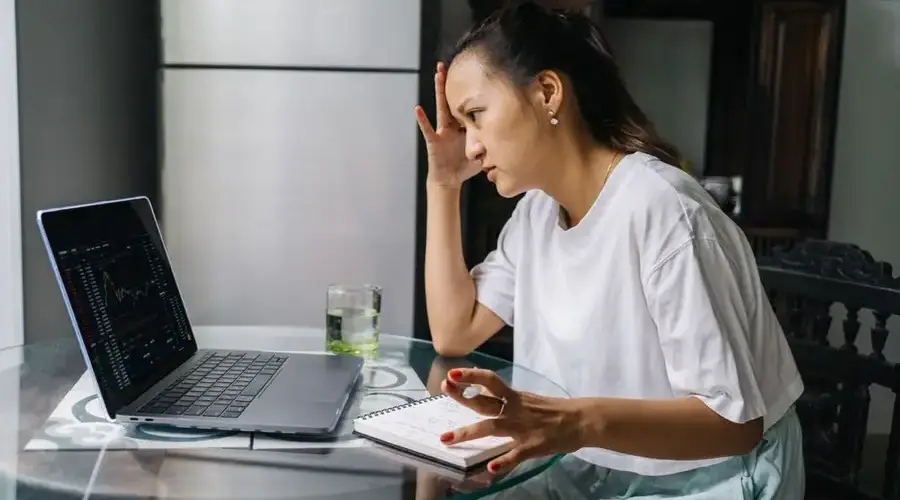 Woman worriedly analyzing stock market data on laptop at home, indicating financial stress.