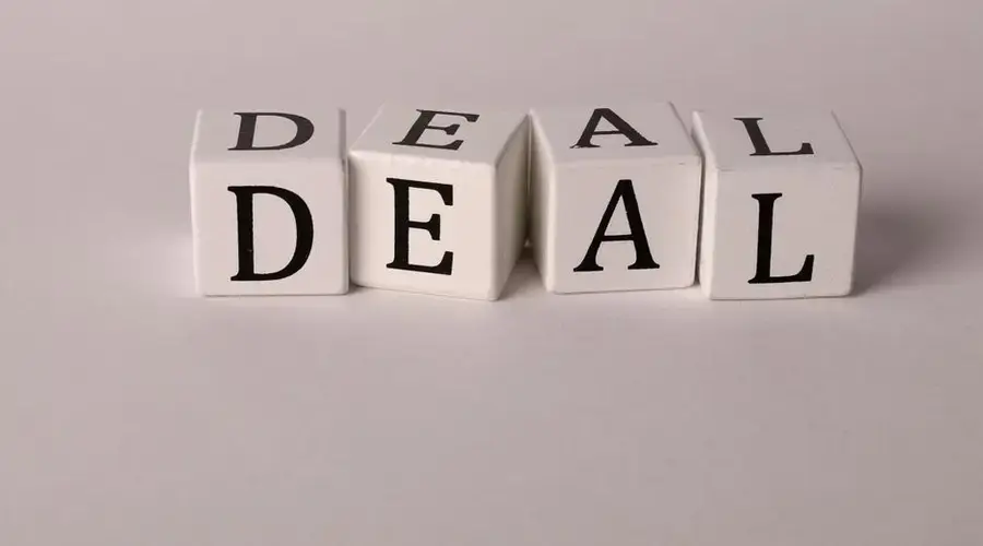 Close-up of white cubes with black letters spelling DEAL on a plain background.