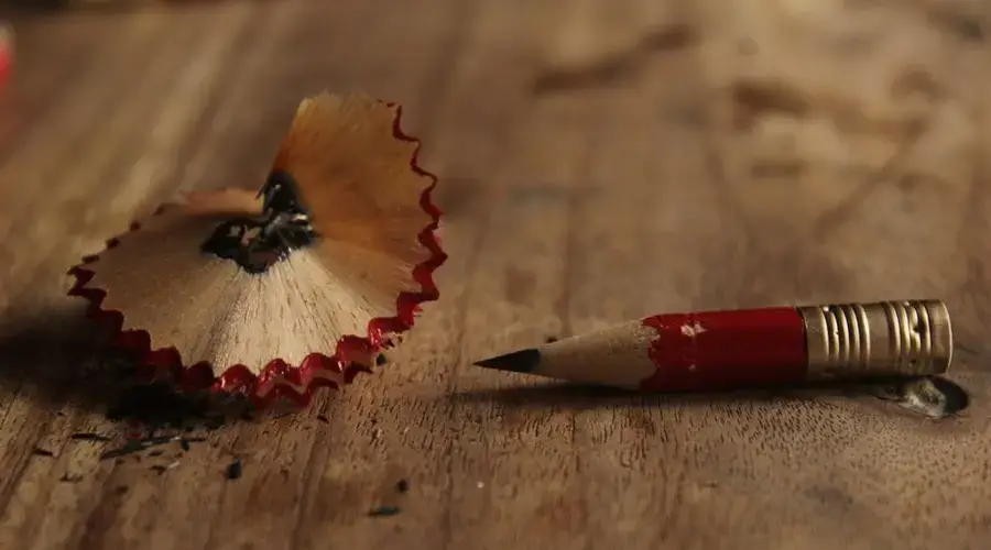 A worn-down red pencil and sharpener shavings on a rustic wooden table.