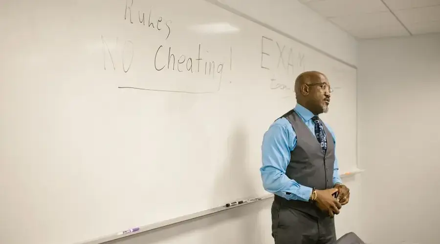 A professor in a classroom emphasizing exam rules on a whiteboard.