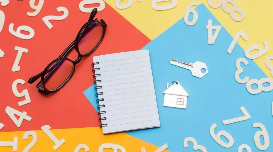 Flat lay of a colorful desktop featuring a notebook, eyeglasses, and house key with numbers scattered.
