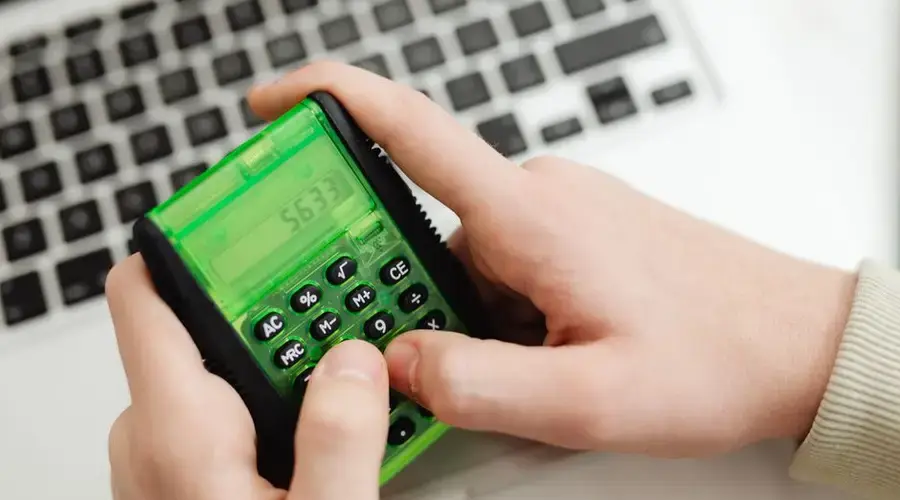 Close-up of hands using a green calculator near a laptop. Modern finance concept.