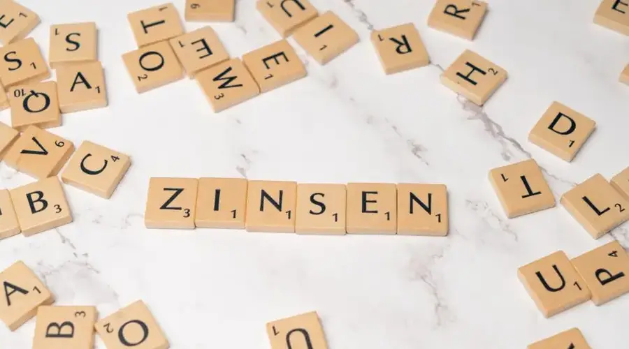 Scrabble tiles spelling 'Zinsen' on a marble surface with scattered tiles around, symbolizing interest rates.