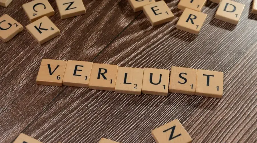 Scrabble tiles spelling 'Verlust' on a wooden table, symbolizing loss or financial context.