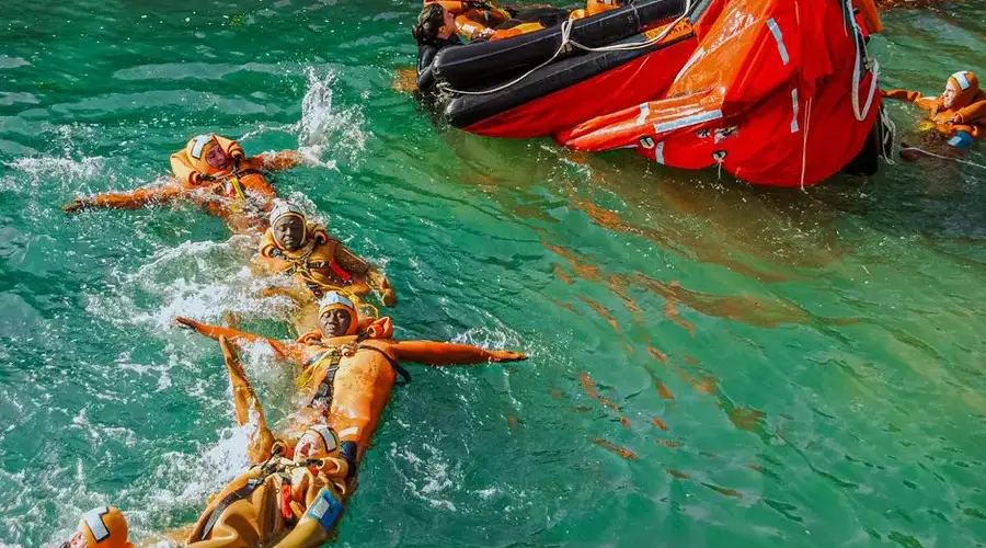 Group of adults practicing lifeboat safety drill in the water wearing life jackets.
