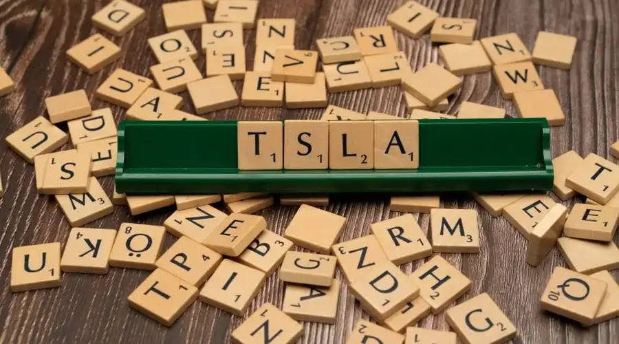Wooden letter tiles spell TSLA, hinting at the stock market and investment themes.