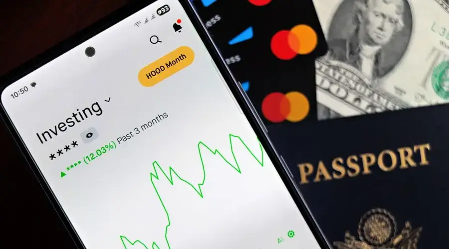 Smartphone showing stock market app with travel essentials: passport, money, and cards.