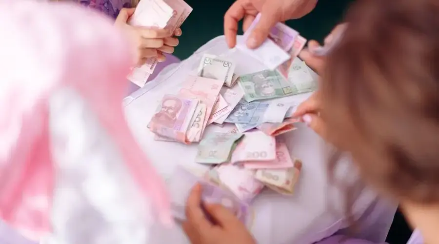 A child and adult hands sorting colorful banknotes on a table, symbolizing financial education.