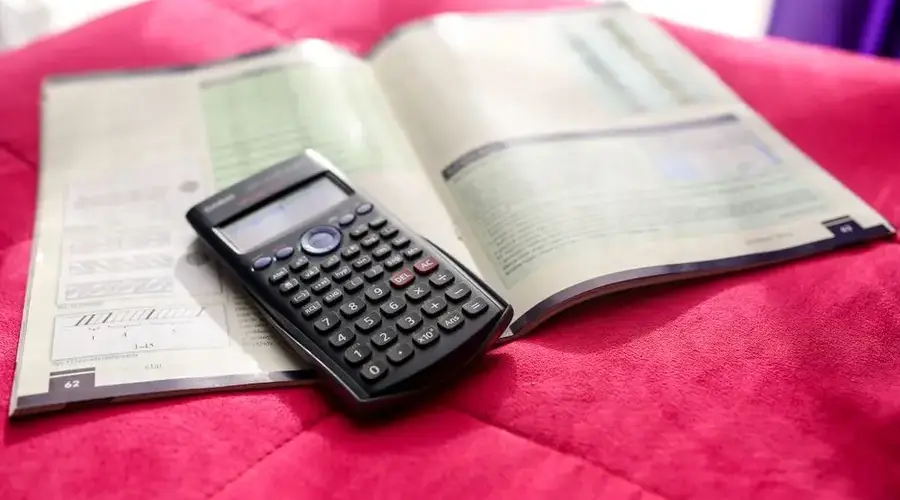 A scientific calculator and open textbook on a vibrant pink surface, ideal for education and academic themes.