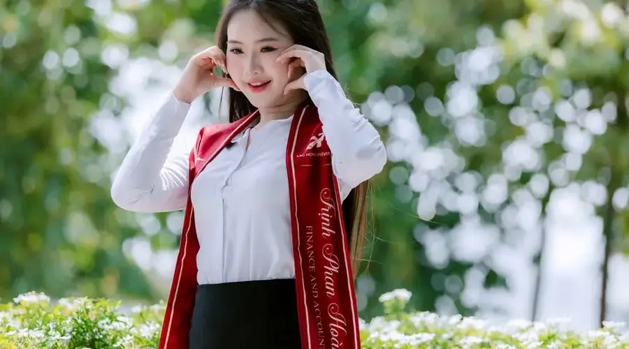 Young woman celebrating graduation outdoors, wearing cap and academic regalia.
