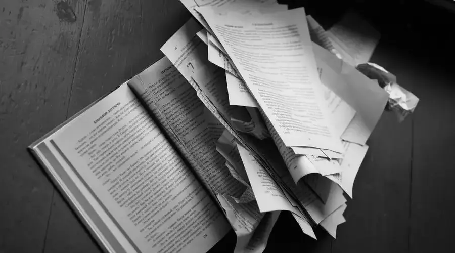 Dramatic black and white image of torn book pages scattered over a wooden floor.