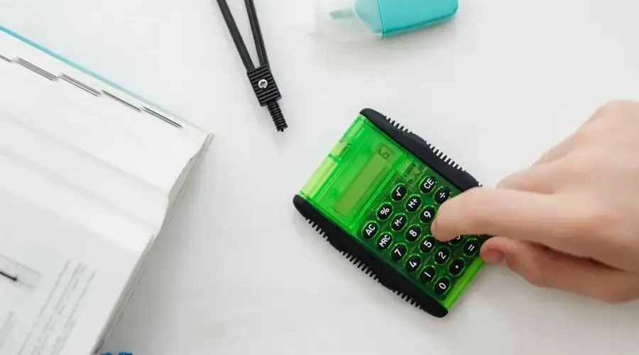 Close-up of a hand using a green calculator with stationery for studies or business calculations.