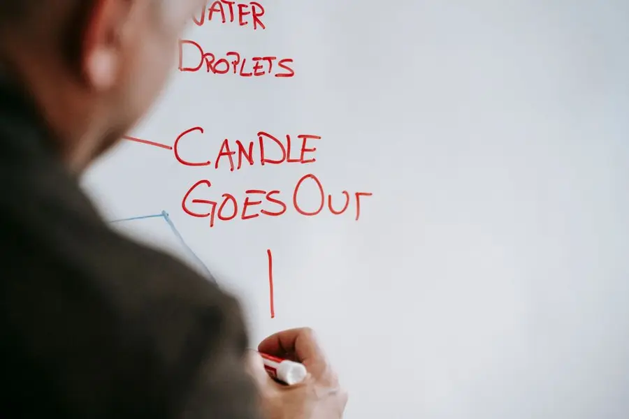 A teacher writes on a whiteboard with red marker in an educational setting.