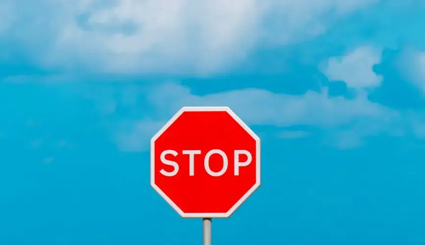Red stop sign with ocean and sky, contrasting colors in outdoor setting.