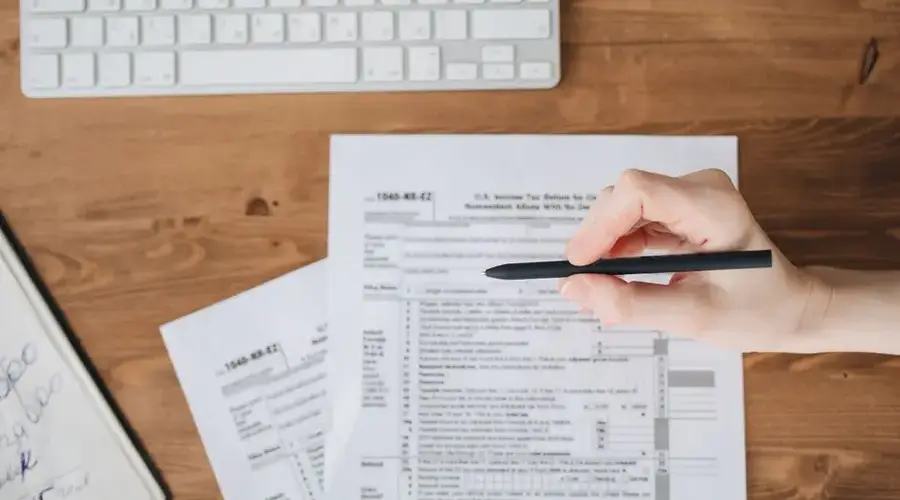 Close-up of a hand holding a pen over US tax forms on a wooden table.