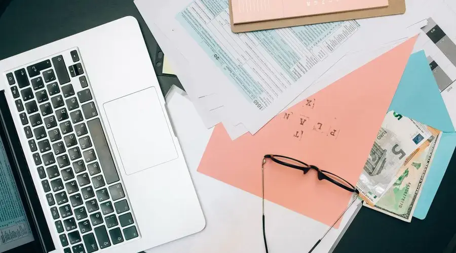 A tidy workspace featuring a laptop, documents, and eyeglasses for productivity.