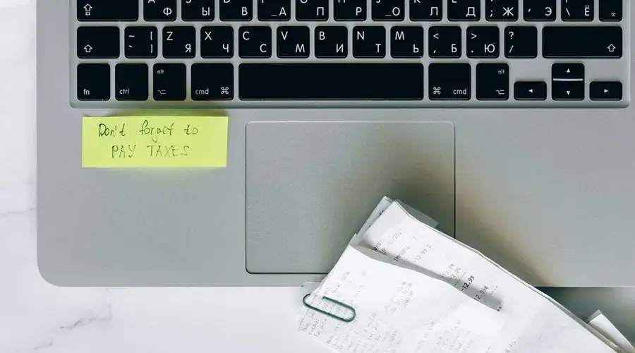 A laptop with a sticky note reminder and receipts, emphasizing tax season organization.
