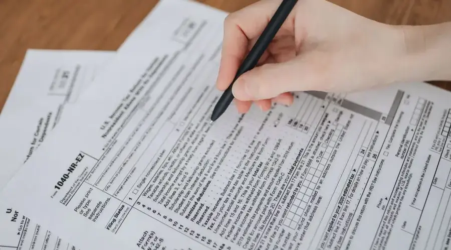 Close-up of a hand writing on tax documents with a black pen.
