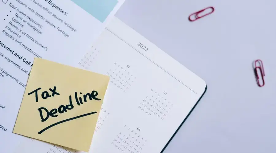 A sticky note highlights tax deadline on a calendar alongside documents, emphasizing financial planning.