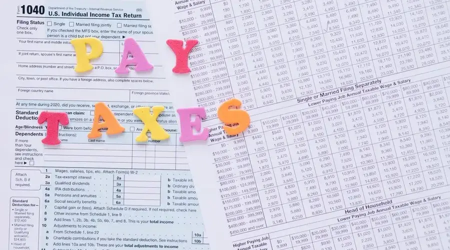 Close-up of U.S. tax forms with colorful 'PAY TAXES' letters emphasizing financial deadlines.