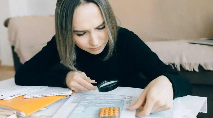 A focused young woman examines documents with a magnifying glass, highlighting attention to detail in accounting tasks.