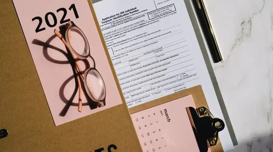 Flat lay of tax forms, calendar, and glasses for 2021 financial planning.
