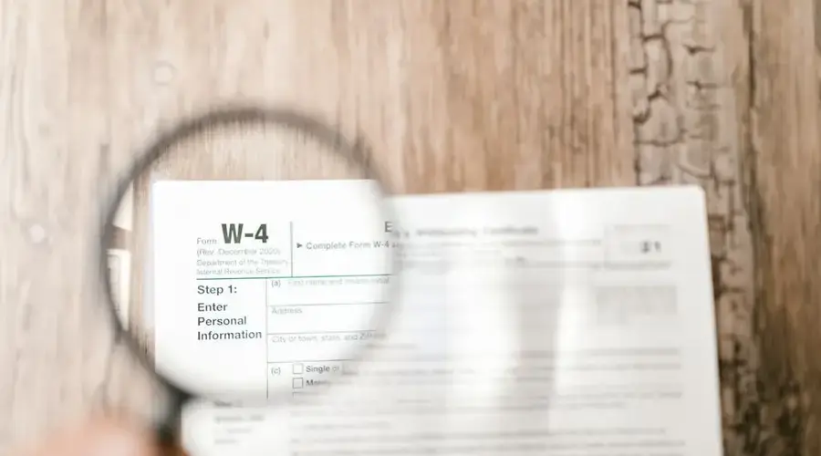 Close-up of a W-4 tax form through a magnifying glass on a wooden table.