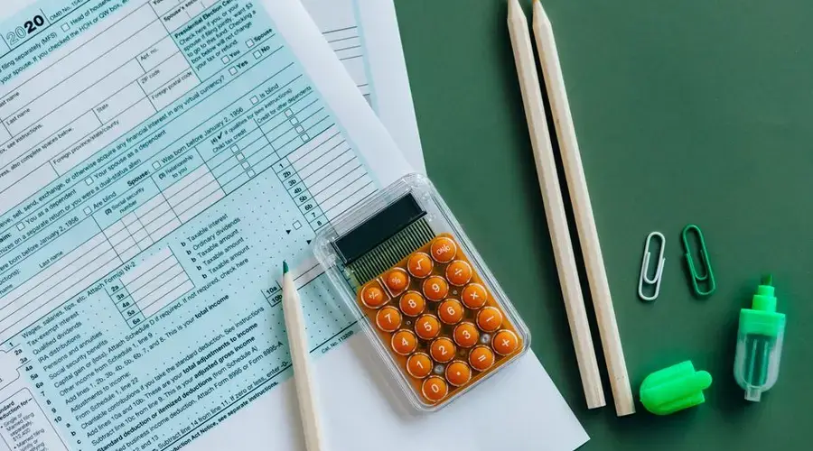 Flat lay of tax forms, calculator, pencils, and clips on green surface, ideal for finance or accounting themes.