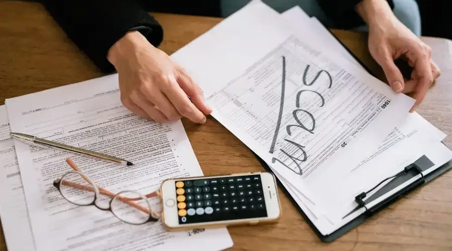 Hands of a person examining tax forms labeled as scam with calculator and papers.