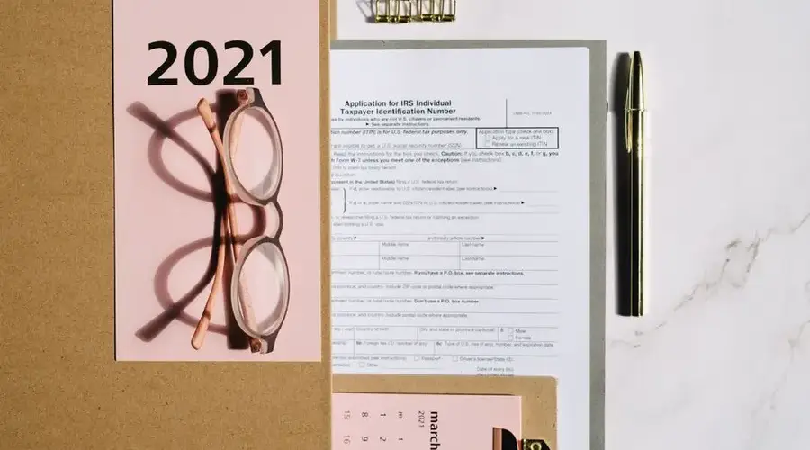 Flat lay image featuring 2021 tax documents, eyeglasses, and office supplies on a marble surface.