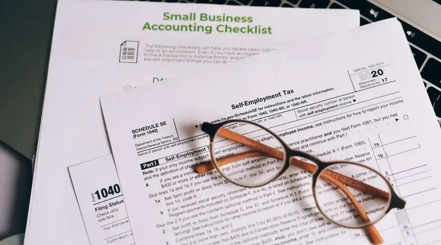 Close-up of tax forms and a small business accounting checklist on a laptop.