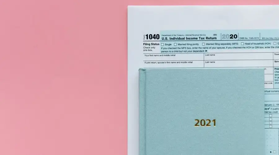 U.S. 1040 tax form with 2021 planner on a pastel pink background, symbolizing tax season.