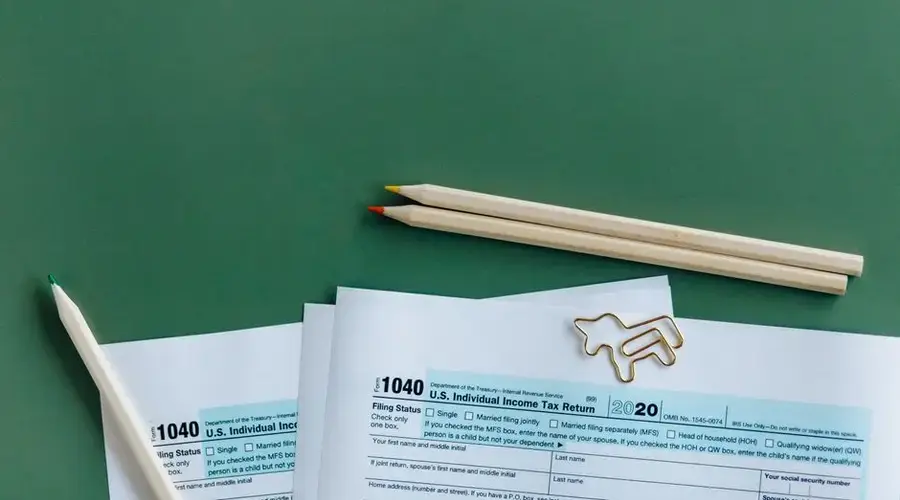 1040 tax form with colored pencils and paperclip on green background.